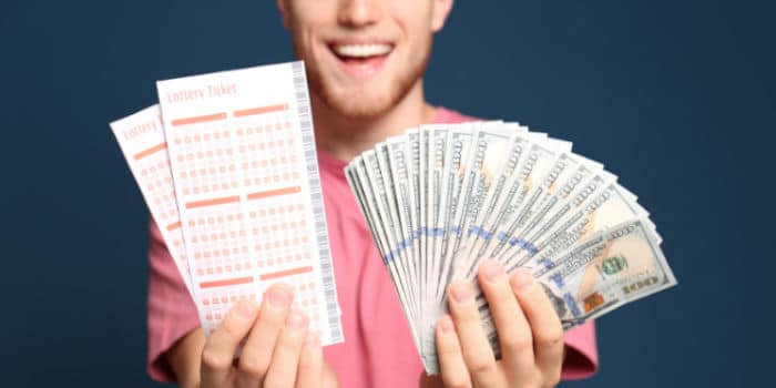 A happy young man holding money and lottery tickets