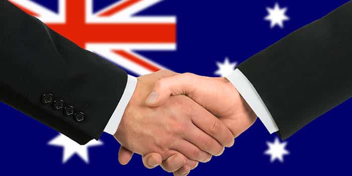 Two businessman shake hands before the flag of Australia