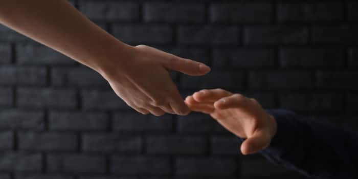 A woman's hand reaching for the hand of a man, symbolizing help and support