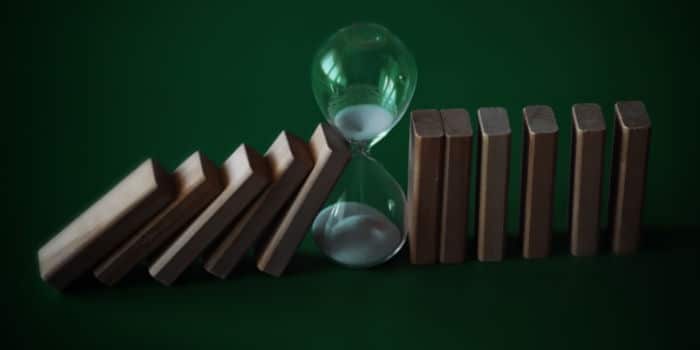 Falling dominoes stopped by a sand clock symbolizing delay