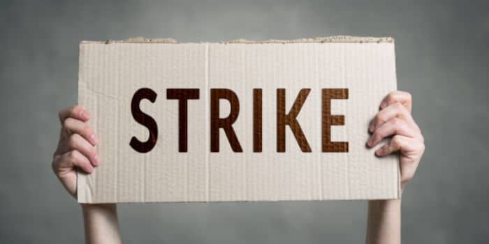 Hands of a person holding a cardboard sign with the word "Strike" written on it